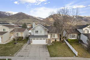 Split level home featuring a garage, concrete driveway, a chimney, a front lawn, and a mountain view