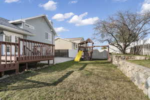Fenced backyard featuring a playground and a wooden deck