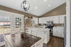 Kitchen with lofted ceiling, stainless steel appliances, white cabinetry, light countertops, and a peninsula
