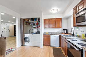 Kitchen with white appliances, wood finish cabinets, washing machine and clothes dryer, light wood-style flooring, and recessed lighting