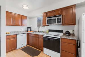 Kitchen featuring white appliances, wood finish cabinetry, and light wood-type flooring