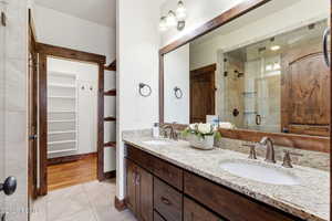 Full bathroom featuring double vanity, a stall shower, a spacious closet, and light tile patterned floors