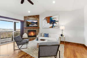 Living room with vaulted ceiling, light wood-style floors, a fireplace, and ceiling fan