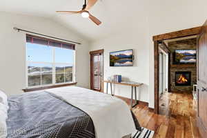 Bedroom featuring lofted ceiling, wood finished floors, a ceiling fan, a stone fireplace, and access to outside