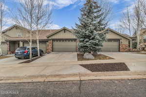 View of front facade featuring stone siding, driveway, roof with shingles, and an attached garage