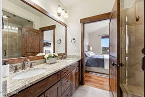 Bathroom featuring a stall shower, double vanity, lofted ceiling, light tile patterned floors, and ensuite bathroom