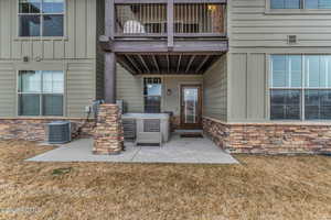 View of exterior entry with stone siding, a patio, board and batten siding, and a yard