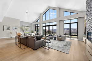 Living room with a stone fireplace, light wood-style flooring, a chandelier, and a high ceiling