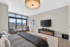 Master bedroom with floor to ceiling windows, access to exterior, light wood finished floors, and a warm lit fireplace