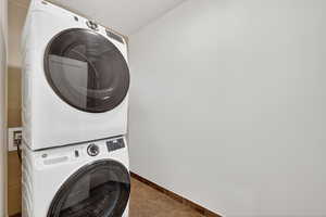 Laundry area featuring stacked washer / dryer and dark tile patterned flooring