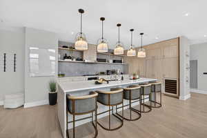 Kitchen featuring open shelves, light wood finish cabinets, wine cooler, a breakfast bar, and a large island