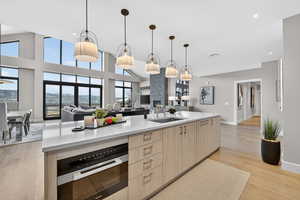 Kitchen with light wood finish cabinetry, light stone countertops, light wood-style floors, decorative light fixtures, and vaulted ceiling
