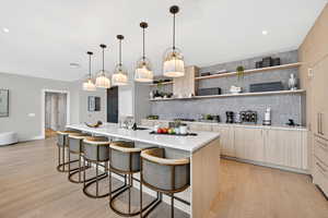 Kitchen with open shelves, light wood finish cabinets, modern cabinets, a breakfast bar, and a large island