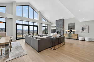 Living room with light wood-type flooring, a stone fireplace, vaulted ceiling, and recessed lighting