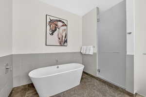 Full bathroom with a soaking tub, tile walls, and a wainscoted wall