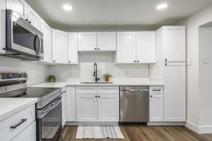 Kitchen with stainless steel appliances, white cabinets, light stone countertops, and recessed lighting