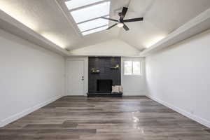 Unfurnished living room featuring ceiling fan, dark wood finished floors, a fireplace, and a textured ceiling