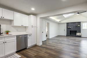 Kitchen with white cabinetry, dark wood-style floors, vaulted ceiling, stainless steel dishwasher, and a ceiling fan