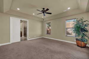 Unfurnished bedroom featuring carpet, ceiling fan, a tray ceiling, recessed lighting, and ensuite bathroom
