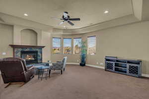 Sitting room featuring a raised ceiling, a ceiling fan, a fireplace, light colored carpet, and recessed lighting