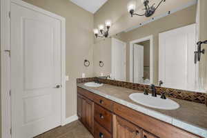 Full bathroom with double vanity, dark tile patterned floors, and a chandelier