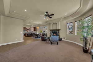 Living room with a raised ceiling, a ceiling fan, recessed lighting, carpet flooring, and a premium fireplace