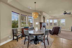 Dining area with a fireplace, ceiling fan, a tray ceiling, light tile patterned floors, and recessed lighting