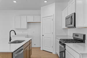 Kitchen featuring stainless steel appliances, light stone countertops, light wood-style flooring, a center island with sink, and white cabinets
