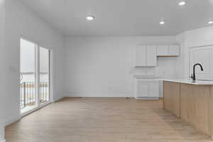 Kitchen featuring two tone cabinetry, light wood-type flooring, recessed lighting, and light stone countertops