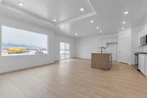 Two tone kitchen with stainless steel appliances, a kitchen island with sink, light wood-style floors, recessed lighting, and two tone cabinets