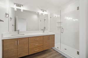 Bathroom featuring double vanity, dark wood-style flooring, and a marble finish shower