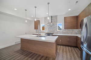 Kitchen with light countertops, pendant lighting, a center island with sink, stainless steel appliances, and dark wood-style floors