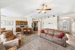 Living room featuring a ceiling fan, vaulted ceiling, arched walkways, light colored carpet, and light tile patterned floors