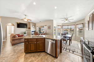 Kitchen with a ceiling fan, stainless steel appliances, open floor plan, a center island with sink, and vaulted ceiling