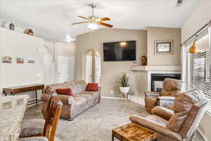 Carpeted living room featuring ceiling fan, a tiled fireplace, and arched walkways