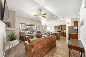 Living room featuring lofted ceiling, a fireplace with raised hearth, and ceiling fan
