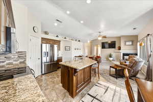 Kitchen featuring open floor plan, light stone countertops, stainless steel appliances, a kitchen breakfast bar, and a fireplace