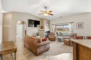 Living room featuring ceiling fan, lofted ceiling, a glass covered fireplace, arched walkways, and light tile patterned flooring