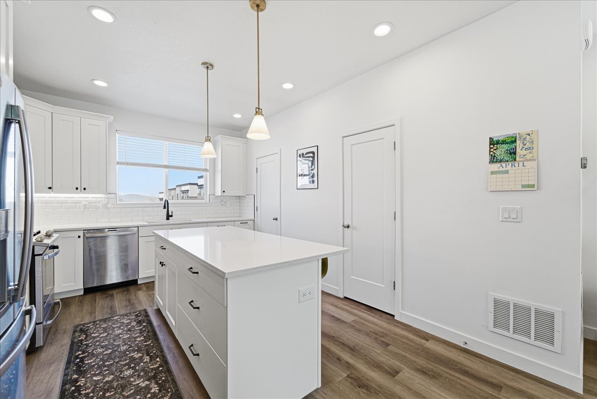 Kitchen featuring white cabinets, dark wood-style flooring, a kitchen island, and stainless steel appliances