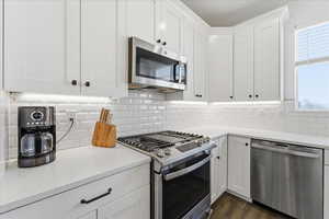 Kitchen featuring stainless steel appliances, white cabinetry, light stone countertops, tasteful backsplash, and dark wood finished floors