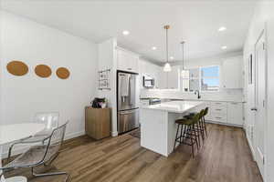 Kitchen with stainless steel appliances, a kitchen island, white cabinetry, a breakfast bar area, and dark wood-type flooring