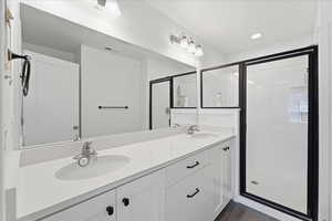 Bathroom featuring a shower stall, double vanity, recessed lighting, and dark wood finished floors