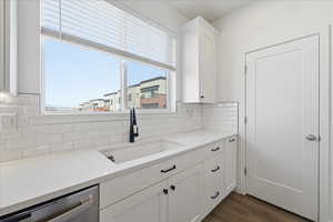 Kitchen featuring white cabinets, light stone counters, dishwasher, dark wood-style floors, and decorative backsplash