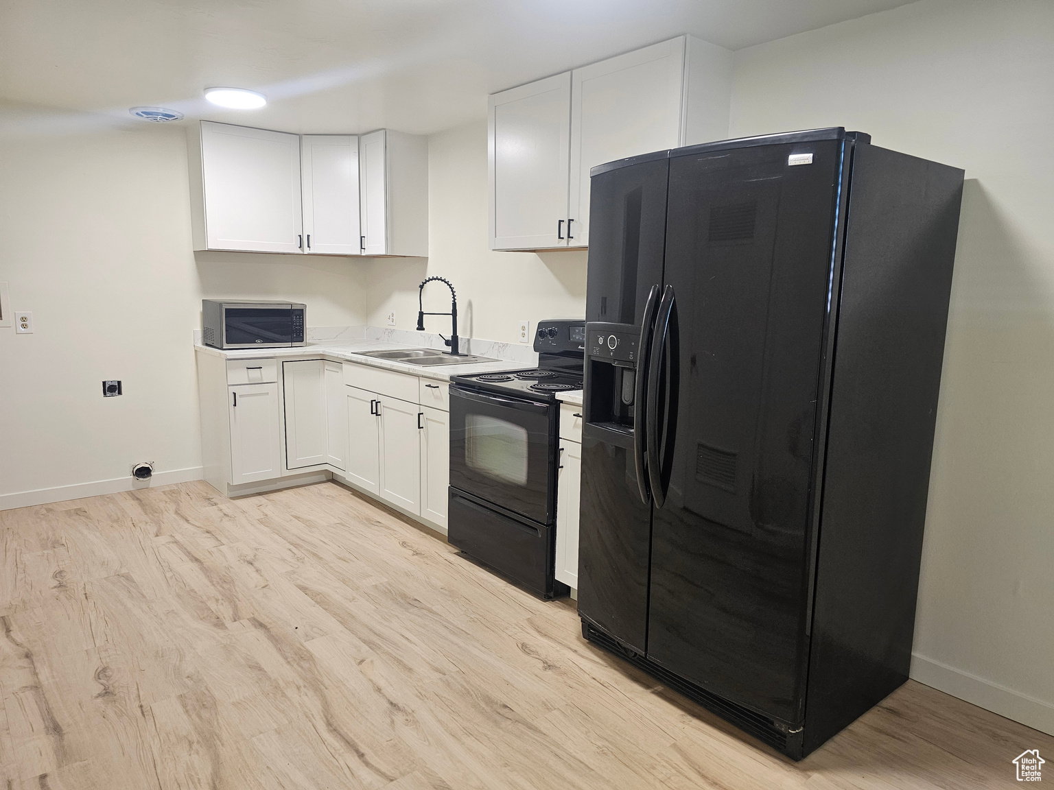 Kitchen featuring black appliances, white cabinets, light countertops, and light wood-style floors