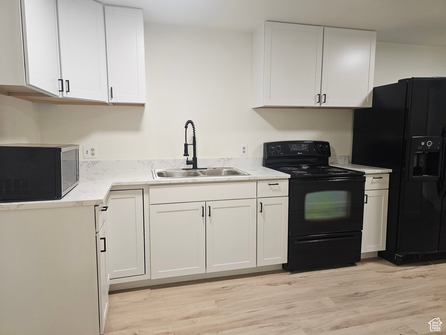 Kitchen with black appliances, white cabinets, light countertops, and light wood-style floors