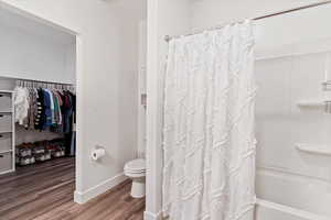 Full bath with wood finished floors, shower / bath combo with shower curtain, and a spacious closet