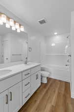 Full bathroom with double vanity, light wood-style flooring, and shower / tub combination
