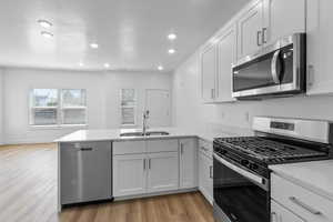 Kitchen with stainless steel appliances, a peninsula, light wood-type flooring, white cabinetry, and light stone countertops