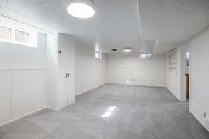 Basement with light colored carpet, healthy amount of natural light, a wainscoted wall  and built in shelves