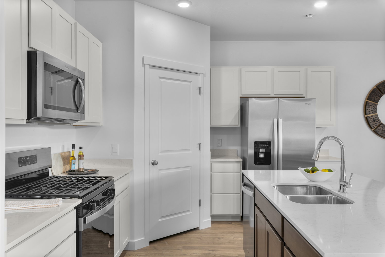 Dual tone kitchen featuring stainless steel appliances, light wood-type flooring, two tone cabinets, and light stone counters
